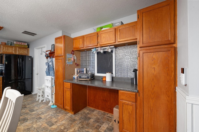 kitchen with built in desk, backsplash, a textured ceiling, and black fridge