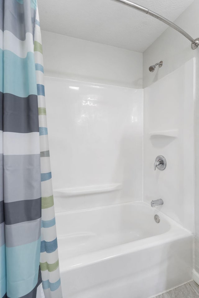 bathroom with shower / bathtub combination with curtain and a textured ceiling