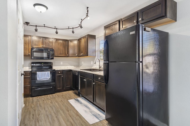 kitchen featuring light wood finished floors, light countertops, a sink, dark brown cabinets, and black appliances