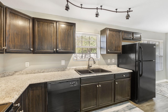 kitchen with dark brown cabinetry, a sink, light wood-style floors, light stone countertops, and black appliances