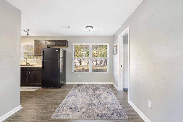 kitchen with dark wood-style floors, dark brown cabinets, a sink, and freestanding refrigerator