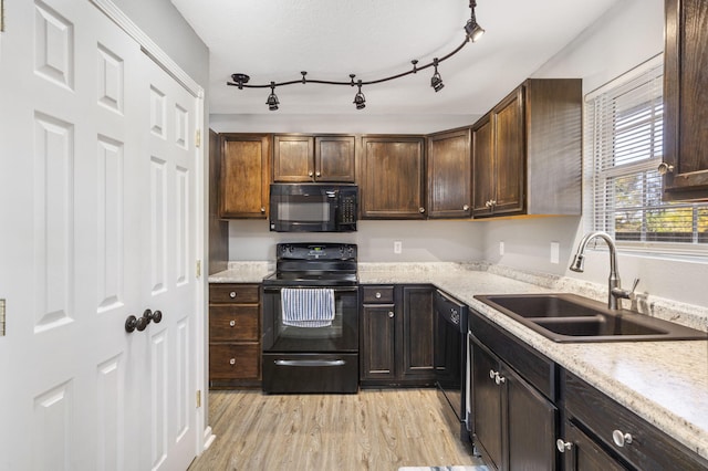 kitchen with light stone counters, dark brown cabinetry, a sink, light wood-style floors, and black appliances