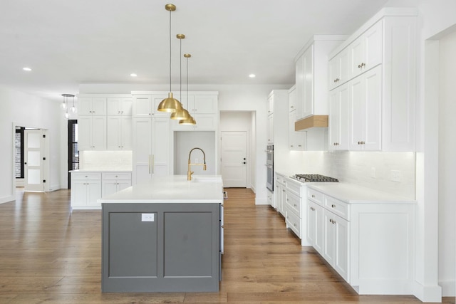 kitchen featuring white cabinetry, tasteful backsplash, hanging light fixtures, and an island with sink