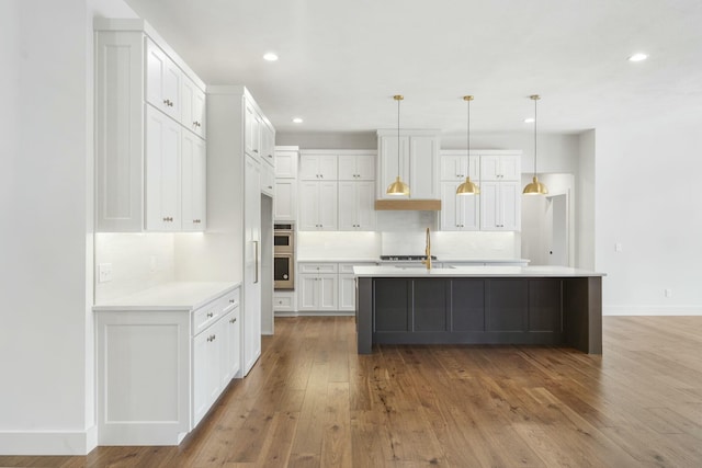 kitchen with hardwood / wood-style floors, an island with sink, decorative backsplash, decorative light fixtures, and white cabinets