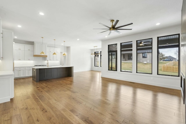 kitchen featuring pendant lighting, white cabinetry, wood-type flooring, an island with sink, and ceiling fan