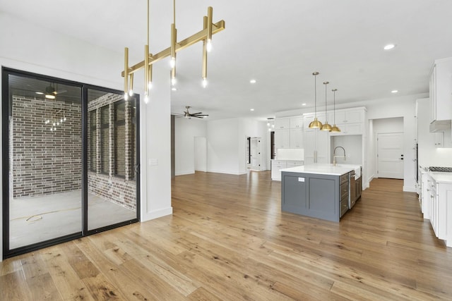 kitchen with ceiling fan, hanging light fixtures, white cabinets, and a center island with sink