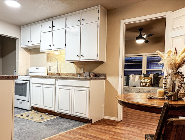 kitchen with dark stone countertops, white cabinets, gas range gas stove, ceiling fan, and light hardwood / wood-style floors