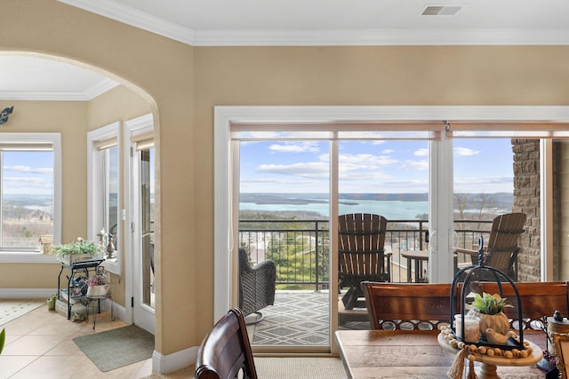 doorway featuring a water view, light tile patterned floors, crown molding, and a healthy amount of sunlight