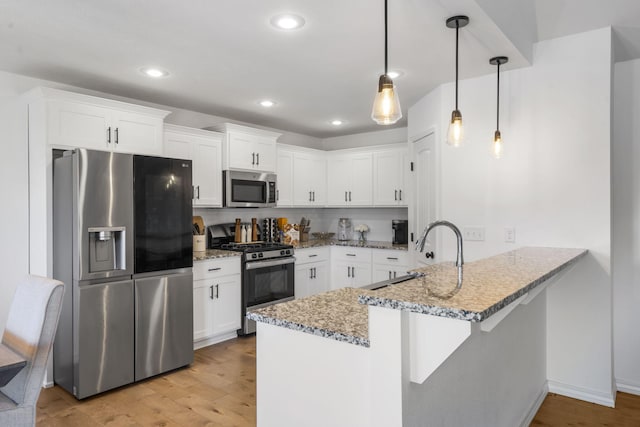 kitchen with kitchen peninsula, appliances with stainless steel finishes, pendant lighting, white cabinets, and sink