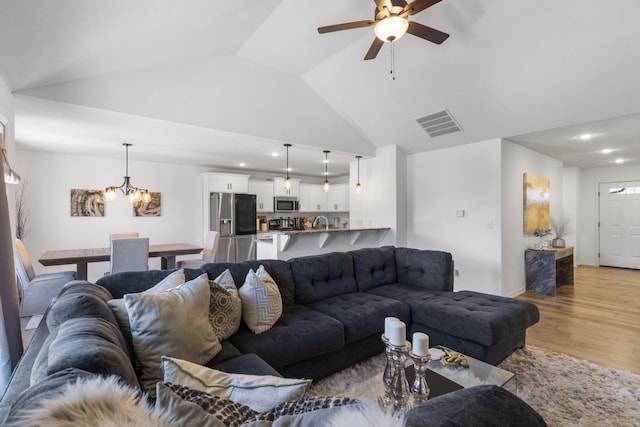 living room featuring lofted ceiling, ceiling fan with notable chandelier, and light hardwood / wood-style flooring