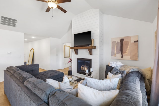 living room with light wood-type flooring, ceiling fan, lofted ceiling, and a fireplace