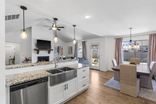 kitchen featuring a large fireplace, stainless steel dishwasher, white cabinets, light stone counters, and sink