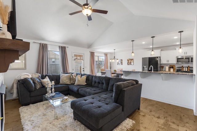 living room featuring lofted ceiling, ceiling fan with notable chandelier, and light hardwood / wood-style flooring