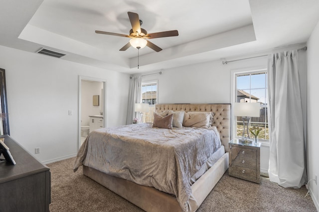 carpeted bedroom featuring ceiling fan, a tray ceiling, and ensuite bath