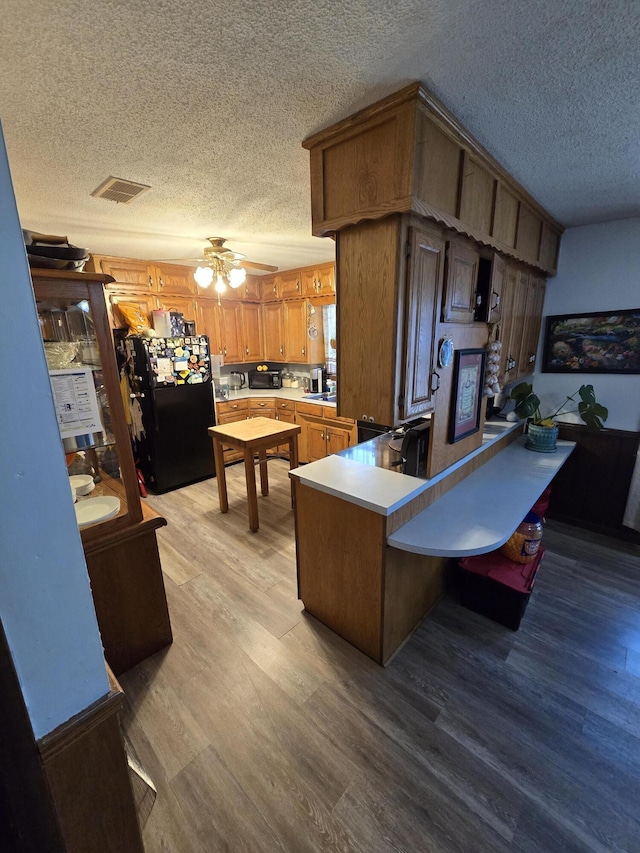 kitchen featuring kitchen peninsula, black fridge, a textured ceiling, light hardwood / wood-style flooring, and a breakfast bar