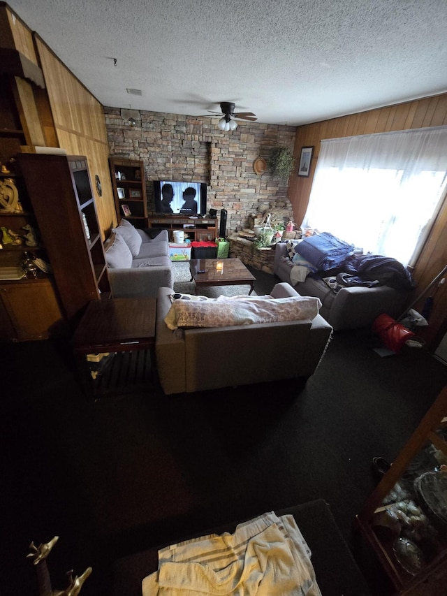 living room featuring ceiling fan, wood walls, and a textured ceiling