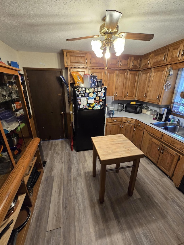 kitchen with ceiling fan, hardwood / wood-style floors, black fridge, sink, and a textured ceiling