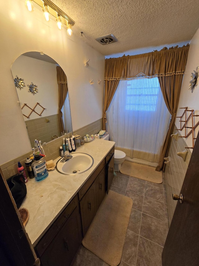 bathroom with toilet, vanity, tile walls, and a textured ceiling