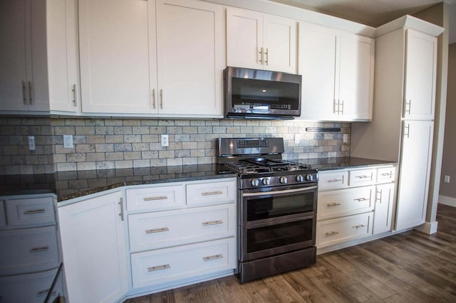 kitchen with backsplash, appliances with stainless steel finishes, dark stone countertops, and white cabinetry