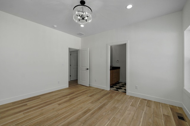 unfurnished bedroom featuring ensuite bath, a notable chandelier, and light hardwood / wood-style floors