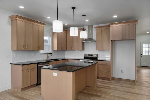 kitchen with appliances with stainless steel finishes, wall chimney exhaust hood, a kitchen island, decorative light fixtures, and sink