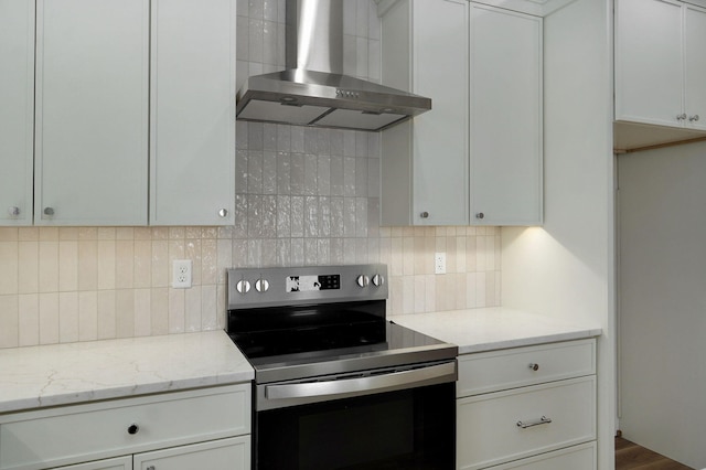 kitchen with backsplash, stainless steel electric range oven, white cabinets, wall chimney exhaust hood, and light stone counters