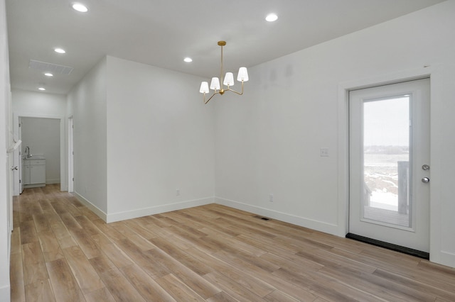 unfurnished dining area featuring light hardwood / wood-style floors, sink, a healthy amount of sunlight, and an inviting chandelier