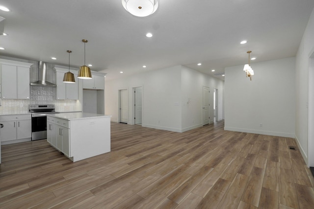 kitchen with electric range, wall chimney range hood, white cabinetry, and pendant lighting