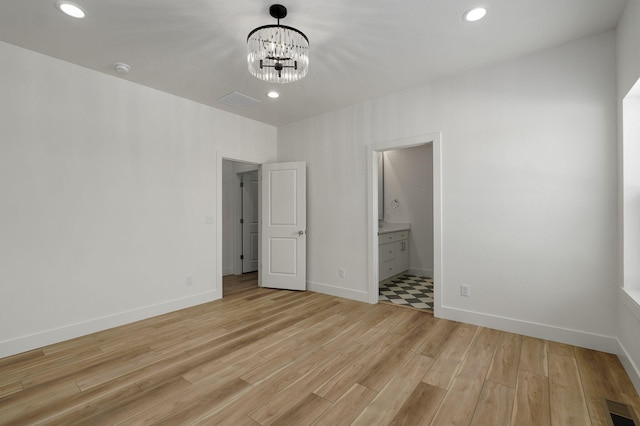 unfurnished bedroom with a notable chandelier, connected bathroom, and light hardwood / wood-style flooring