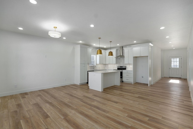 kitchen featuring stainless steel electric stove, a center island, wall chimney exhaust hood, white cabinetry, and hanging light fixtures