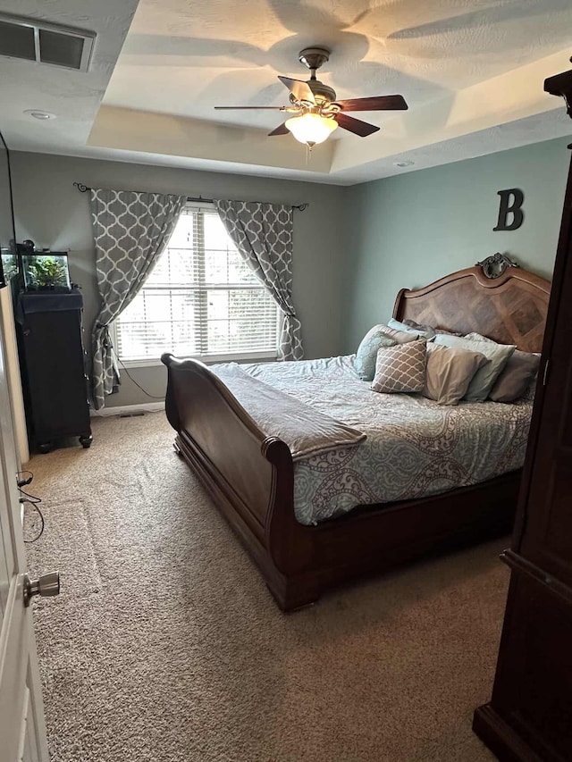 carpeted bedroom featuring a raised ceiling and ceiling fan