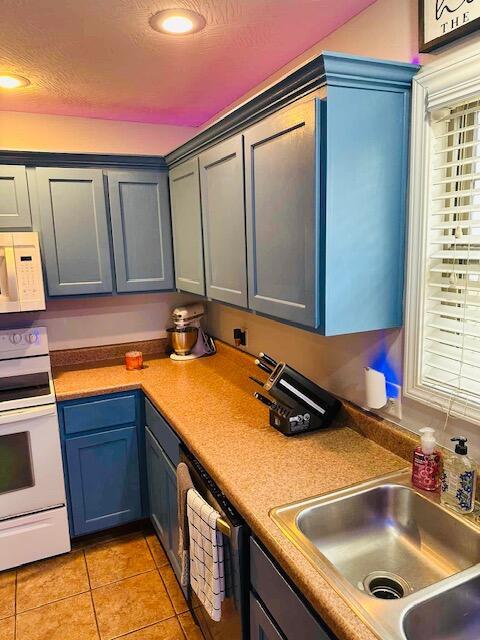 kitchen featuring sink, light tile patterned floors, a textured ceiling, and white appliances