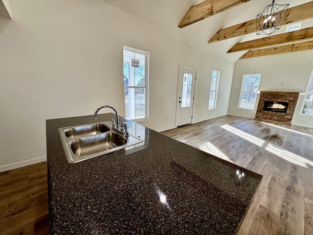 kitchen with dark stone countertops, sink, hanging light fixtures, hardwood / wood-style flooring, and beam ceiling