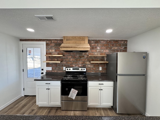 kitchen with a textured ceiling, brick wall, stainless steel appliances, and white cabinets