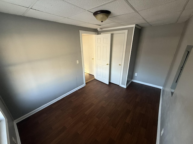 unfurnished bedroom featuring a paneled ceiling, a closet, and dark hardwood / wood-style floors