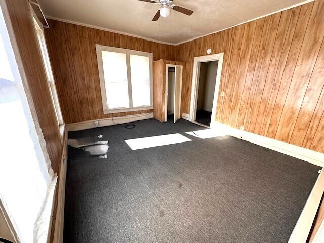 unfurnished room featuring dark colored carpet, ornamental molding, ceiling fan, and wood walls