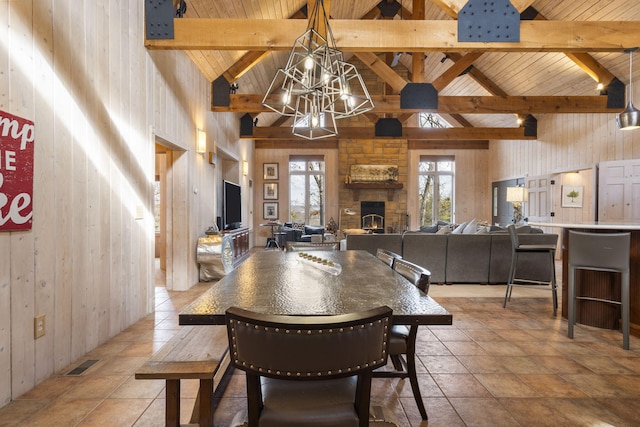 dining room featuring wood walls, a notable chandelier, a fireplace, high vaulted ceiling, and beamed ceiling