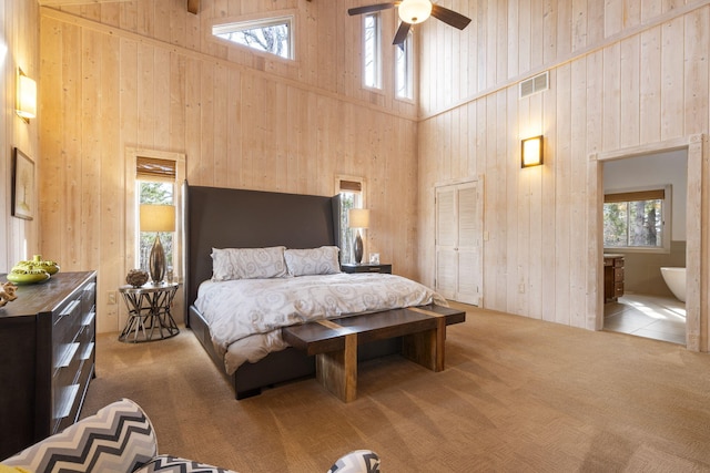 carpeted bedroom with ceiling fan, wood walls, a high ceiling, and multiple windows