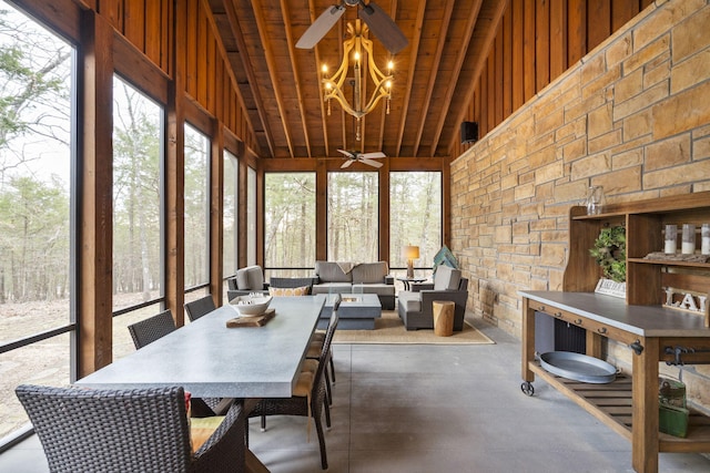 sunroom with ceiling fan with notable chandelier, plenty of natural light, and lofted ceiling