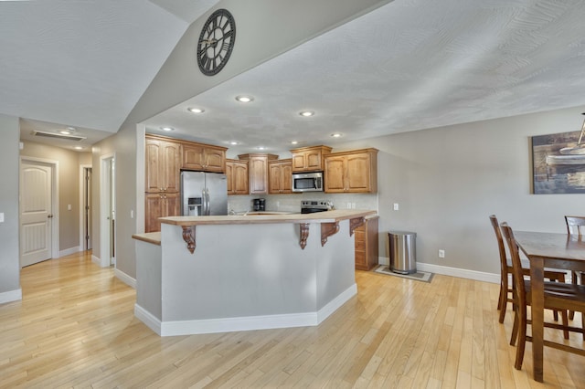 kitchen featuring light hardwood / wood-style floors, a breakfast bar, backsplash, and appliances with stainless steel finishes