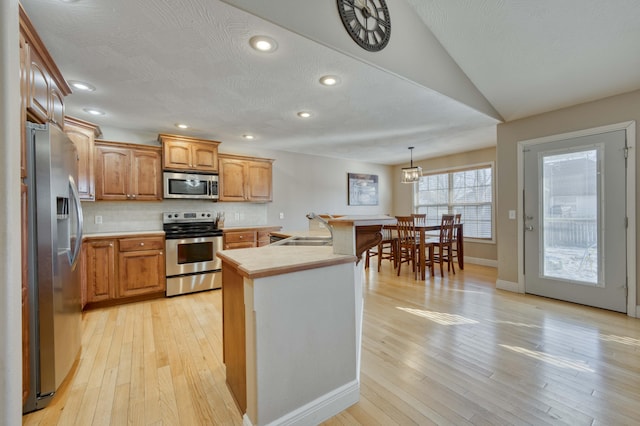 kitchen with tasteful backsplash, light hardwood / wood-style floors, pendant lighting, sink, and appliances with stainless steel finishes