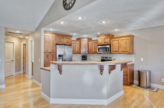 kitchen with stainless steel appliances, decorative backsplash, a kitchen bar, and light hardwood / wood-style flooring