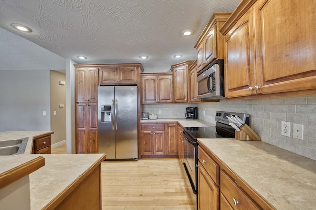 kitchen with tasteful backsplash, sink, light hardwood / wood-style flooring, appliances with stainless steel finishes, and a textured ceiling