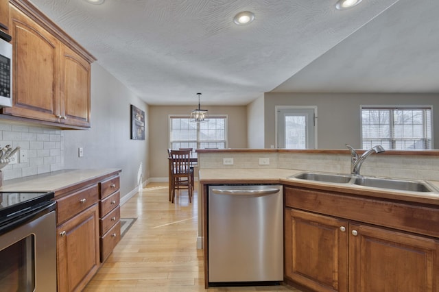 kitchen with light hardwood / wood-style floors, stainless steel appliances, decorative backsplash, decorative light fixtures, and sink