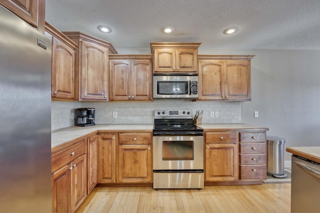 kitchen with backsplash, light wood-type flooring, and appliances with stainless steel finishes