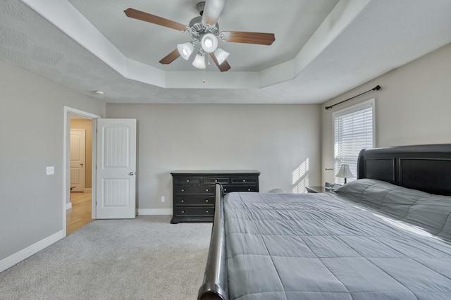 carpeted bedroom with ceiling fan and a raised ceiling