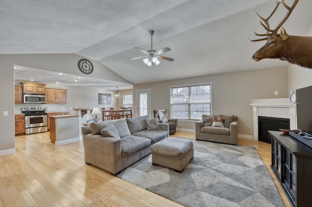 living room with ceiling fan, light wood-type flooring, a textured ceiling, a fireplace, and vaulted ceiling