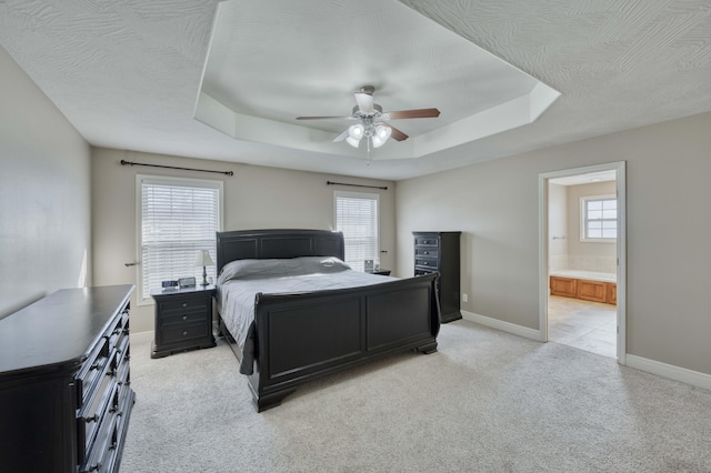 carpeted bedroom with ceiling fan, connected bathroom, a tray ceiling, and a textured ceiling