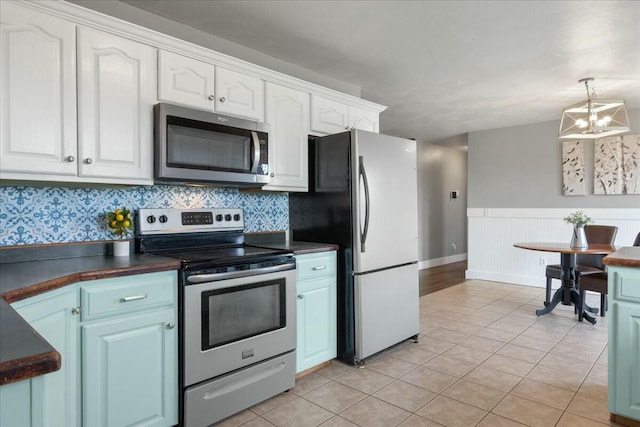 kitchen with light tile patterned floors, stainless steel appliances, white cabinets, and a notable chandelier