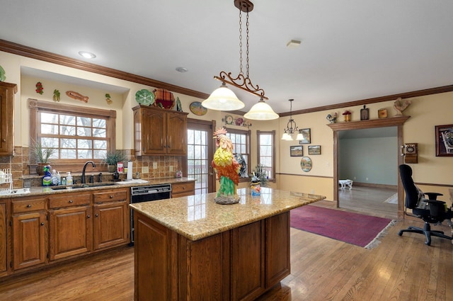 kitchen featuring decorative light fixtures, a kitchen island, sink, black dishwasher, and light hardwood / wood-style flooring